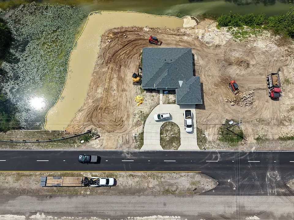 Aerial view of a new house on a filled canal lot with loaders and muddy water