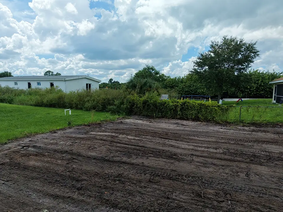 Cleared dirt lot with track marks next to a green lawn and hedge line