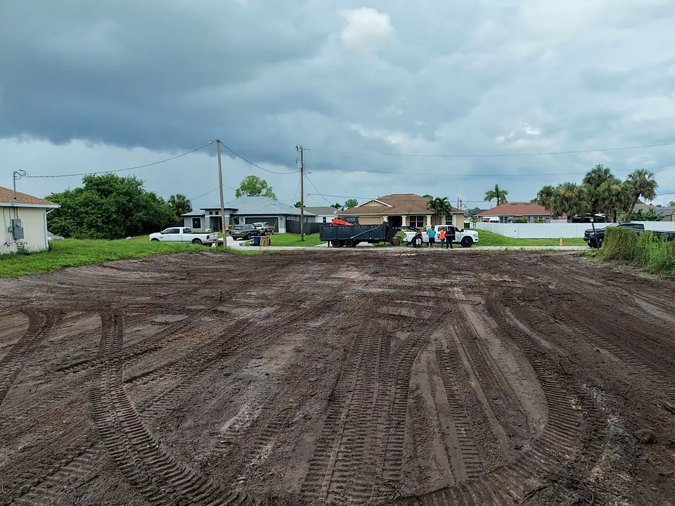 Cleared dirt lot with curved tire tracks leading toward a street with parked trucks