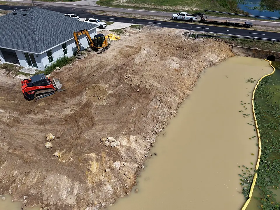 Aerial view of an excavator and track loader working fill along a canal bank