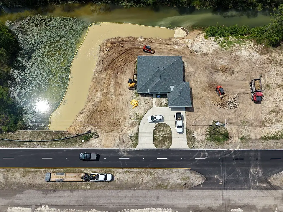 Aerial view of a new house on a filled canal lot with loaders and muddy water