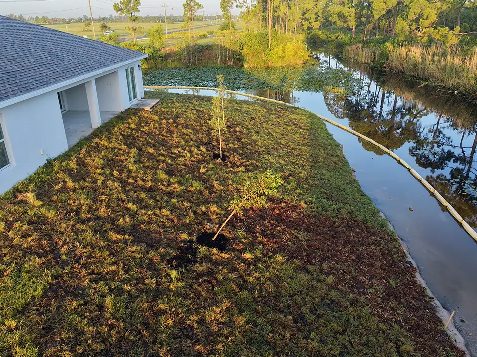 Aerial view of new sod and young trees behind a house along a canal with turbidity barrier