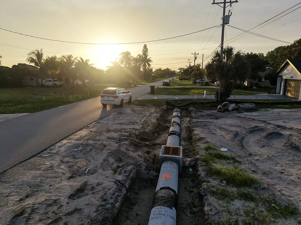 Concrete pipe sections laid in a trench along a street at sunset