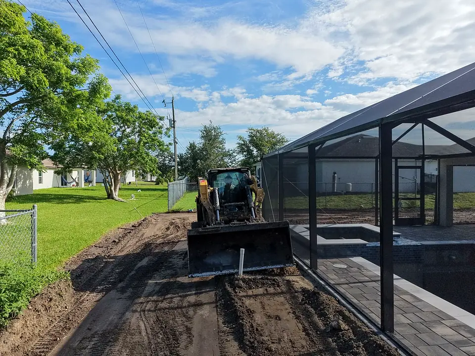 Yellow track loader with blade beside a screened pool enclosure and fence